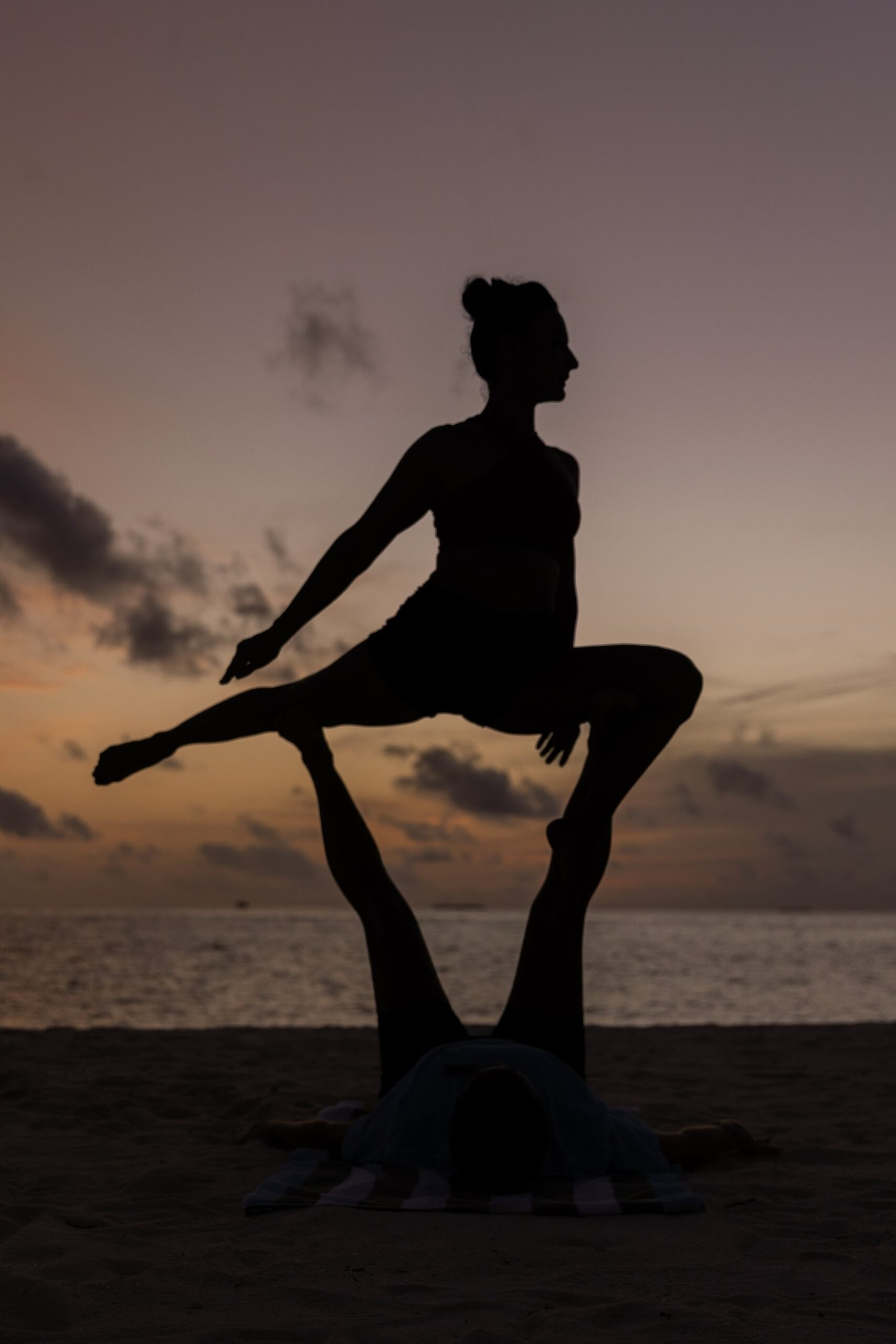 Two people balancing in a partner yoga pose, silhouetted at sunset