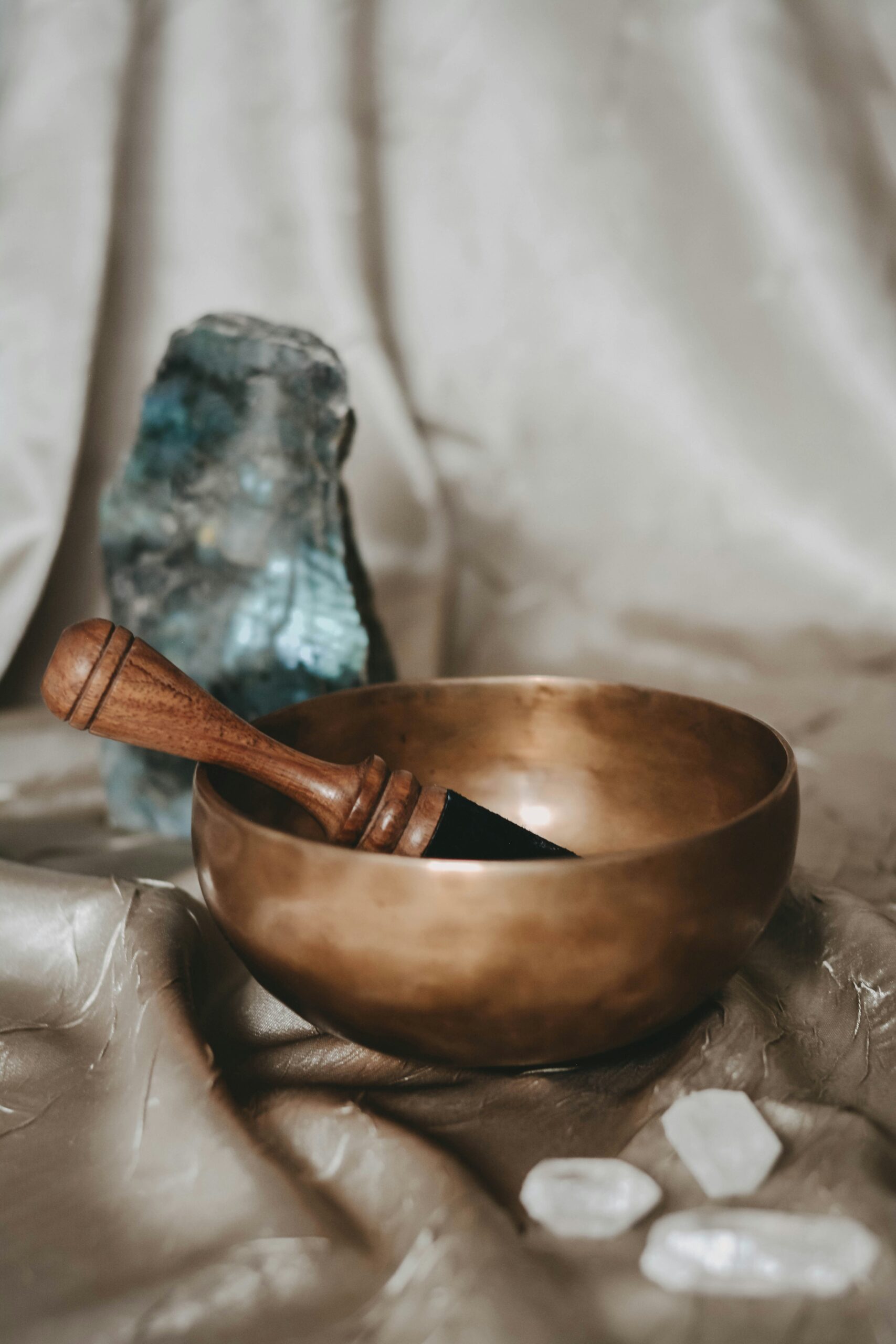 Brass singing bowl with a wooden mallet and quartz crystals on linen