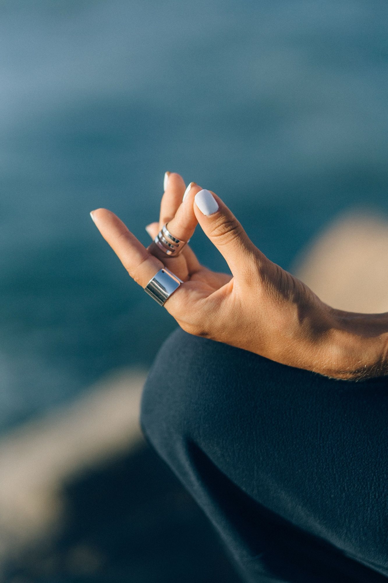 A hand resting in a meditation mudra with the ocean behind