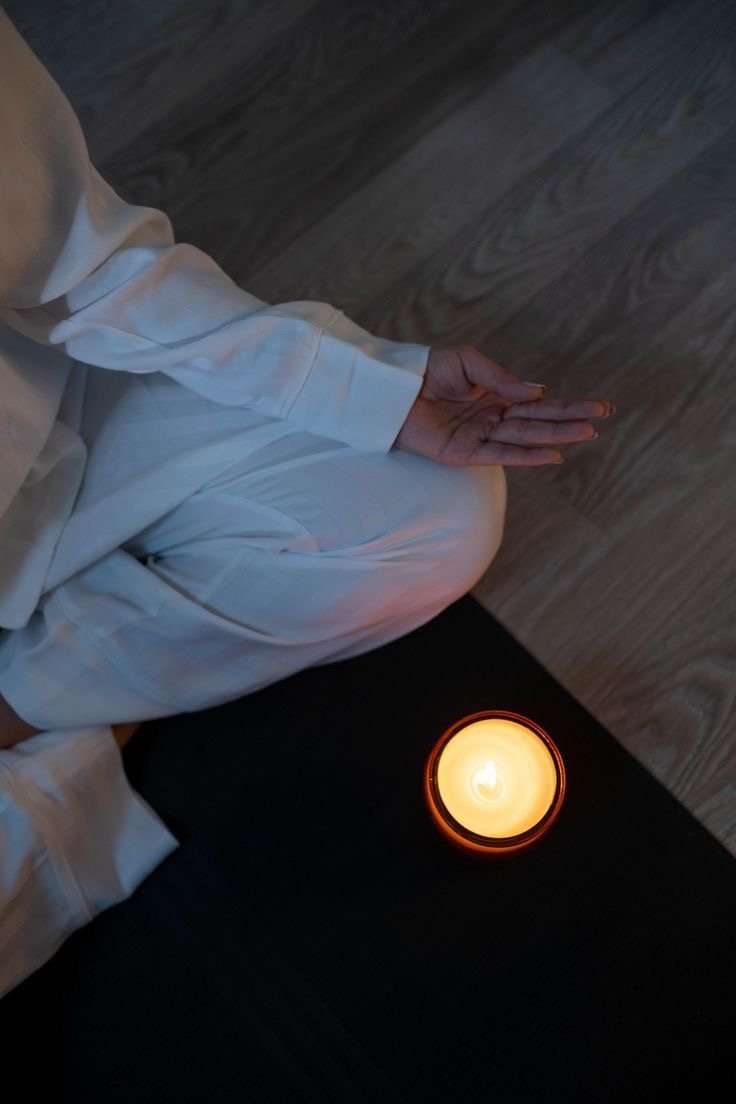 A person in white meditating beside a lit candle