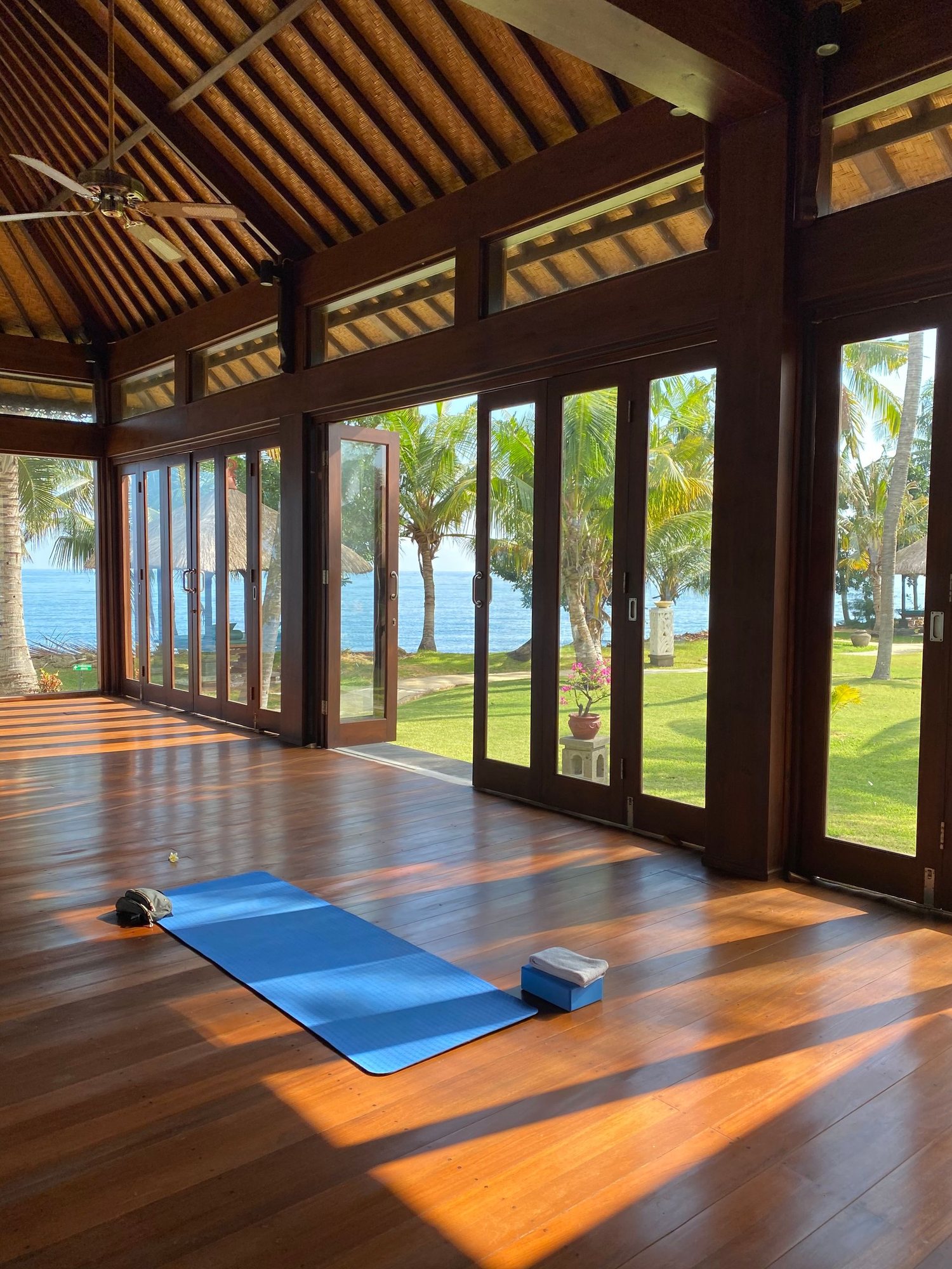 An open timber yoga shala looking out to palm trees and the sea