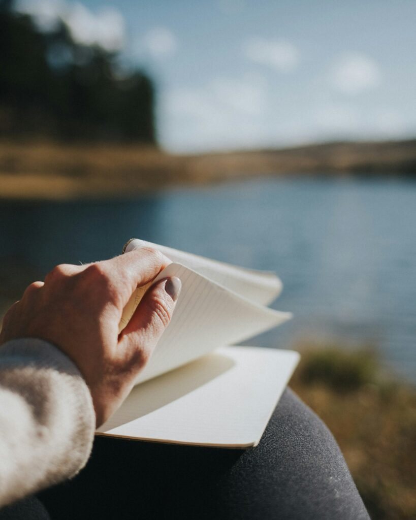 Hands holding an open journal beside a lake