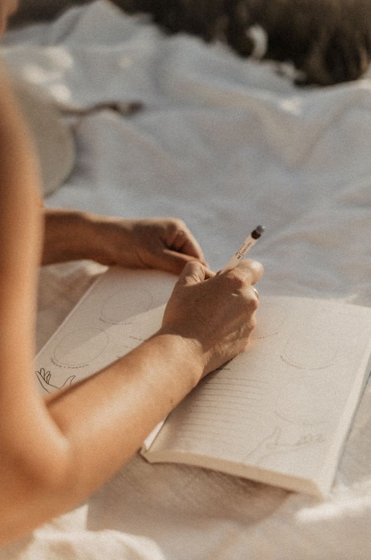 Hands writing in a journal on soft white linen