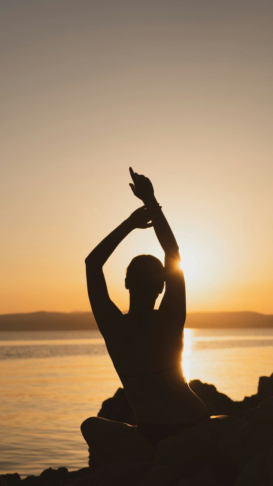 Silhouette with arms raised beside the sea at sunset