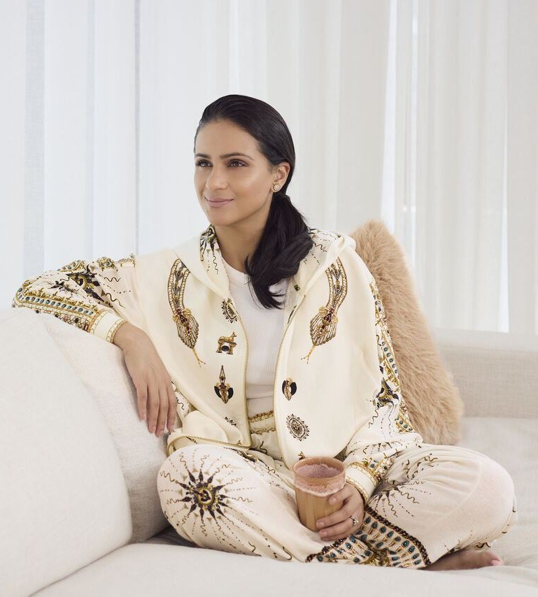 Esha Oberoi sitting on a cream sofa, holding a warm drink