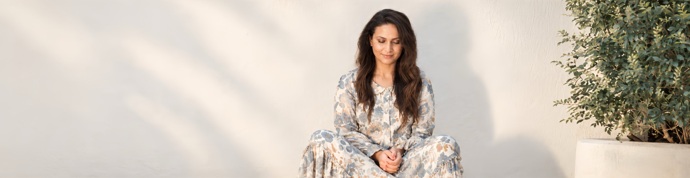 Esha Oberoi sitting on a low wall beside a potted plant