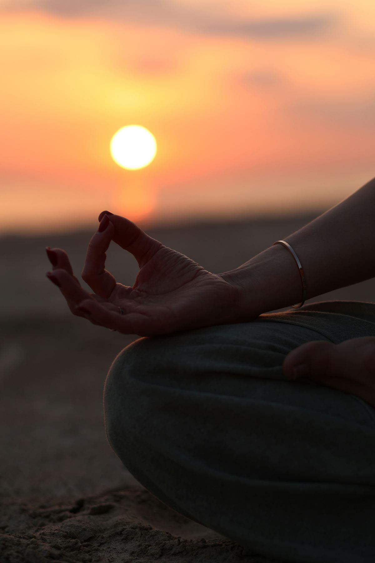A hand resting in a meditation mudra at sunset