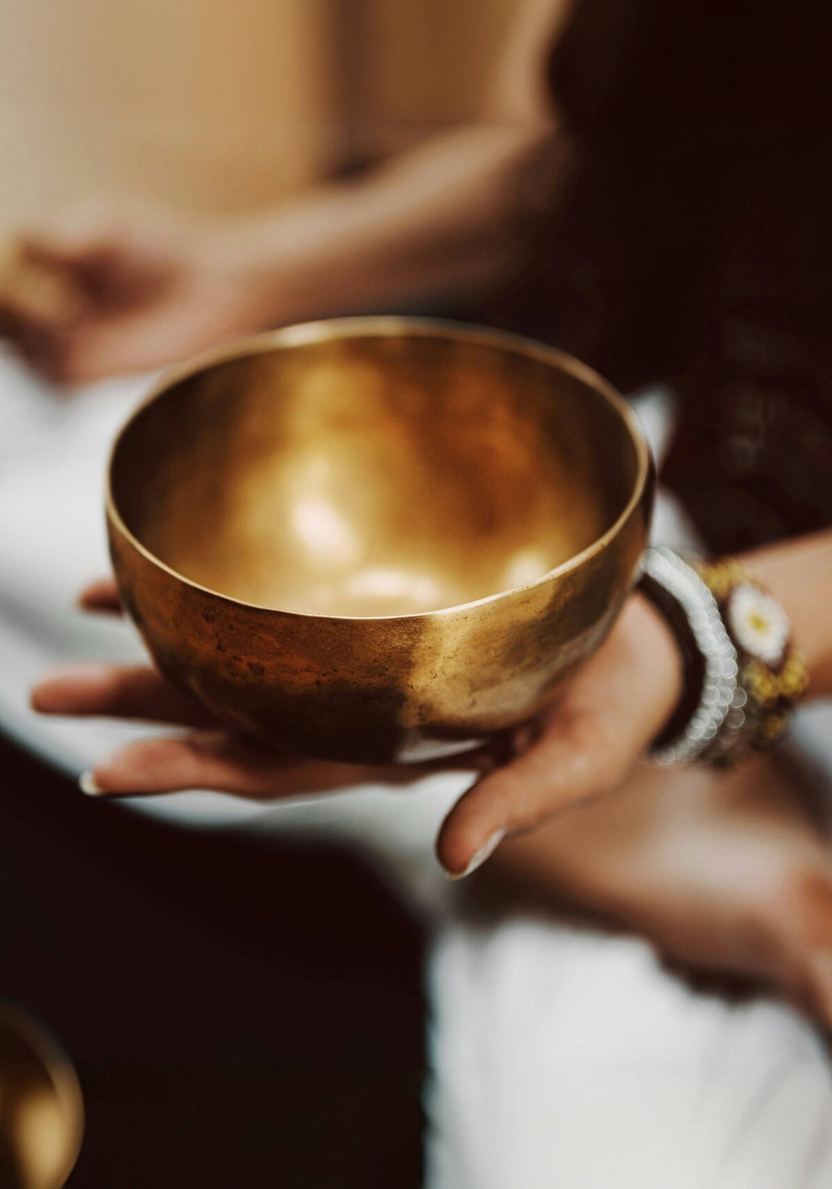 Hands holding a brass singing bowl and wooden striker